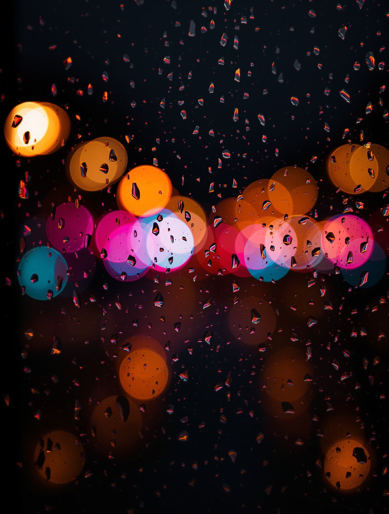 Rain on a dark window with large magenta, cyan and amber bokeh lights behind.