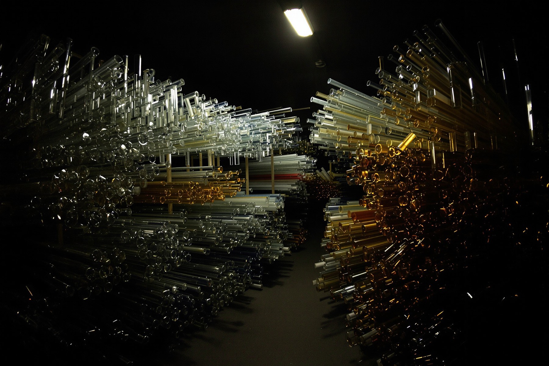 Racks of clear and colored glass tubing stored in a dim workshop.